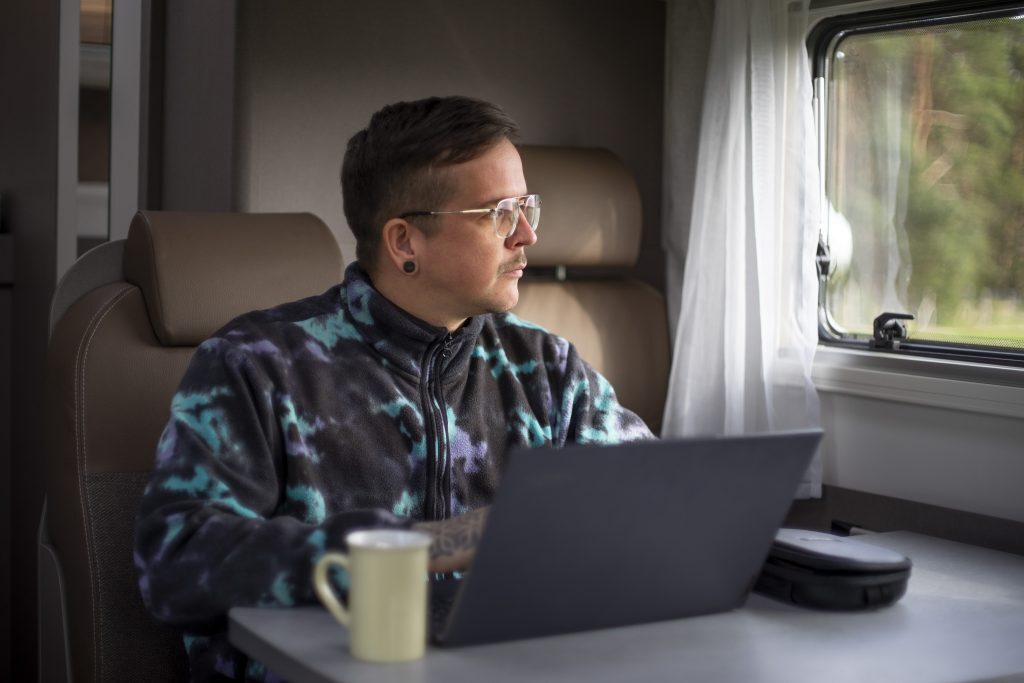 Mann im Wohnwagen mit Laptop und Kaffee
